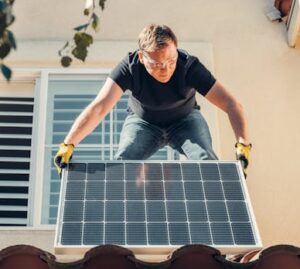 A man in safety glasses installs a solar panel on a house roof, promoting renewable energy.